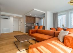 Living room with an orange sofa, kitchen, and wooden decor flooring in the apartment construction project.