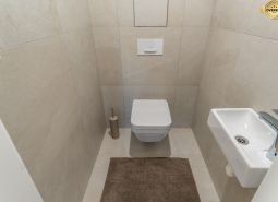 Toilet with a wall-hung toilet, small sink, and beige tiles, Apartment construction.
