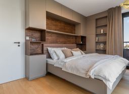 A bedroom in an apartment with modern cabinets and a wooden decor floor.