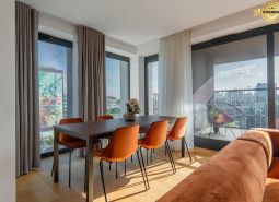 Dining area with orange chairs, wooden decor flooring, access to the balcony. Apartment construction.