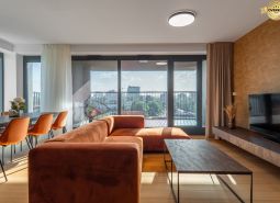 Living room with an orange sofa, dining table, and a view of the city. Apartment construction.