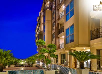 Nighttime construction of apartments in Pattaya with illuminated balconies and green surrounding landscaping.
