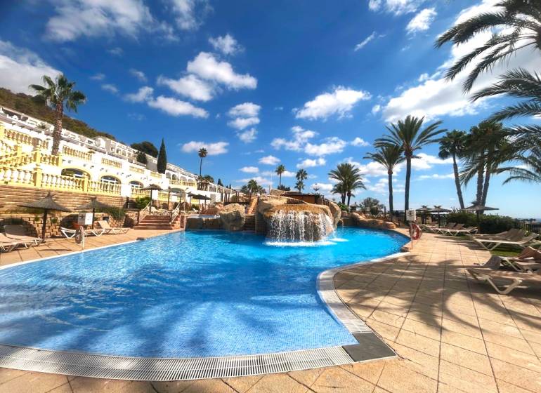 A pool with a waterfall surrounded by palm trees and loungers in a holiday apartment in Calpe.