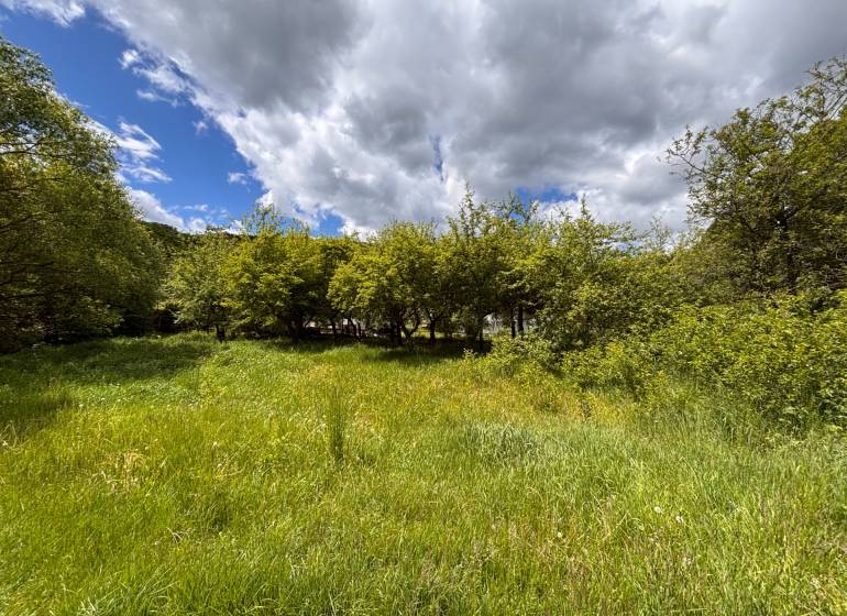 Gardens in Baška near Myslavská Street surrounded by lush greenery and clouds.