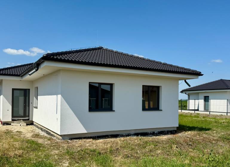 A family house in Mostová with a dark roof on a grassy plot on a sunny day.