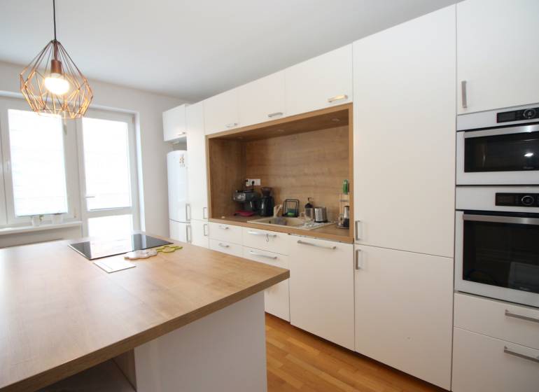 A kitchen in a 2-room apartment with built-in appliances, white cabinets, and wooden flooring.