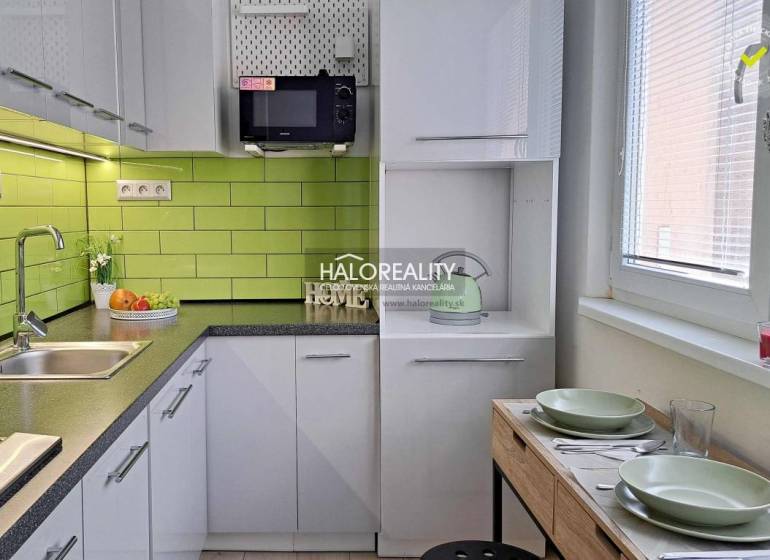 A kitchen in a studio apartment with white cabinets and green tiles.