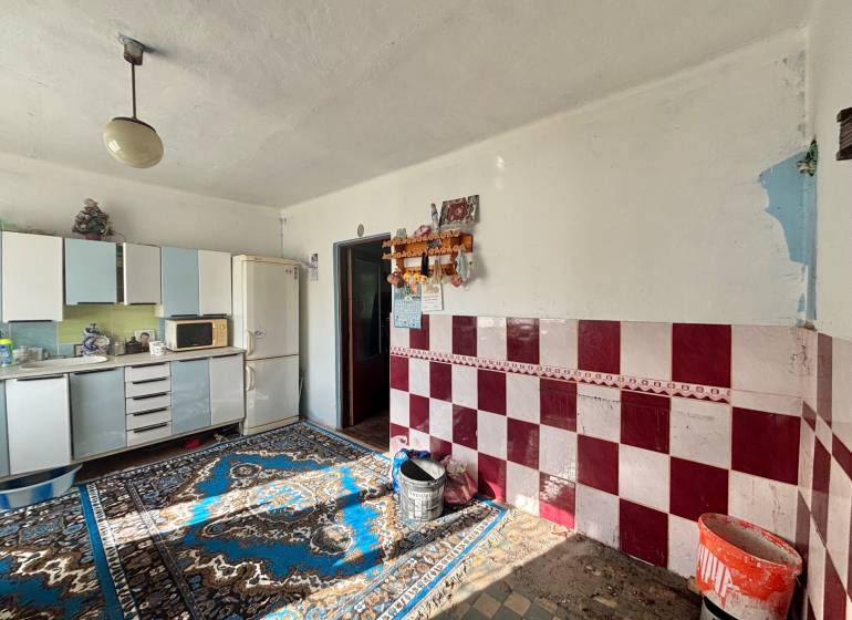 A kitchen in a family house with carpets, white cabinets, and red and white tiles.