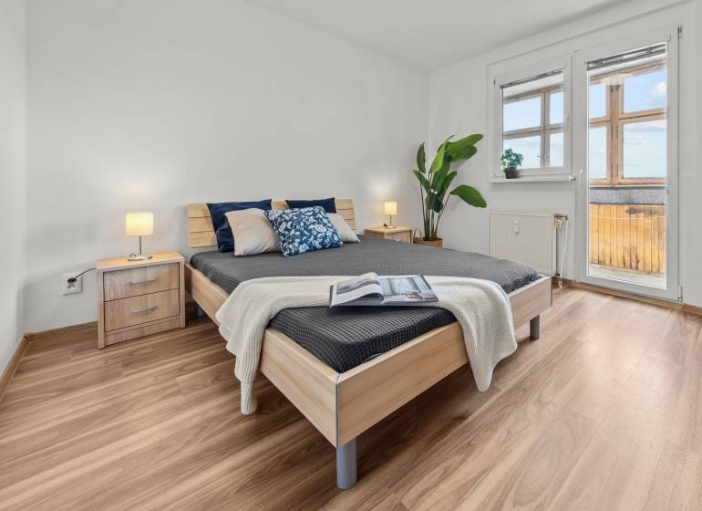 Bedroom with a large bed, nightstand, plant, and a view of the balcony, 3-room apartment.