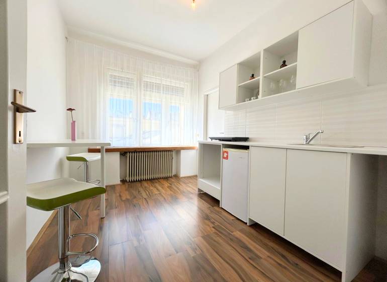 A bright kitchen in a 2-room apartment with laminate flooring and white cabinets.