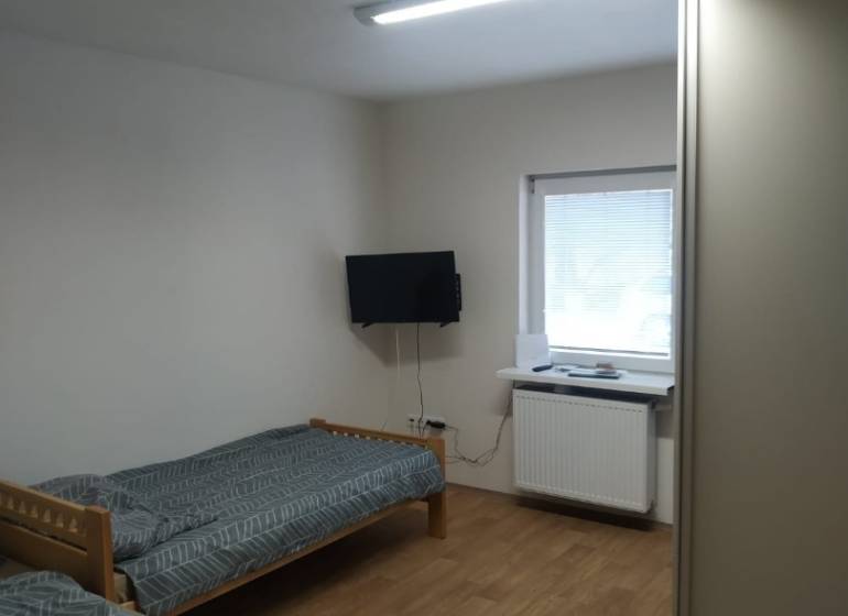 Studio with two beds, a television, and a radiator, light flooring, simple decor.