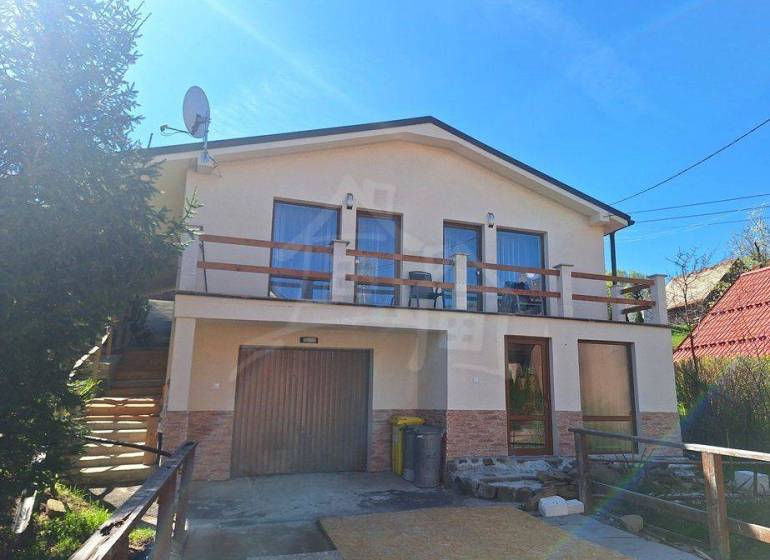 A family house in Liptovský Mikuláš with a balcony and a garage, surrounded by greenery.