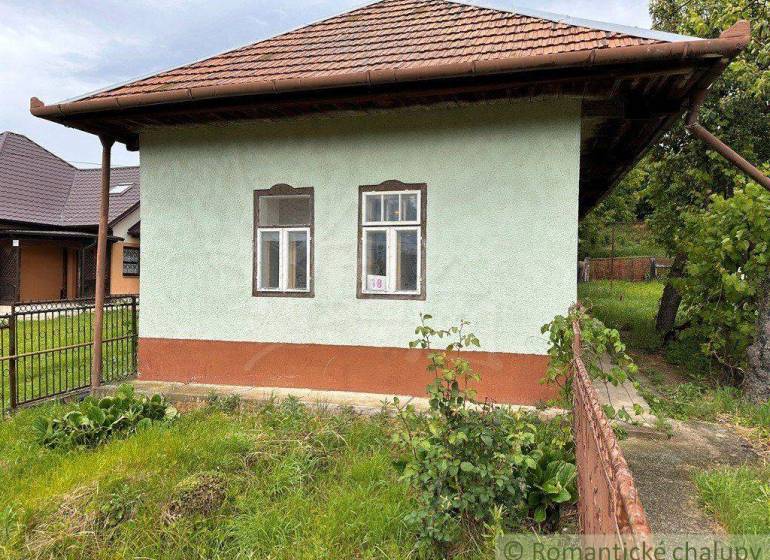 A cottage in Nové Zámky with a green facade and a sloped roof, surrounded by greenery.