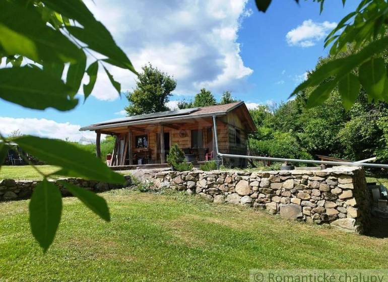 A wooden cottage in Veľký Krtíš surrounded by greenery and a stone wall.
