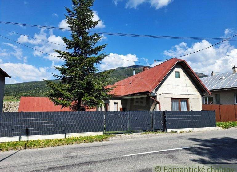 A family house in Telgárt with a red roof, a tall tree, a fence, and a road.