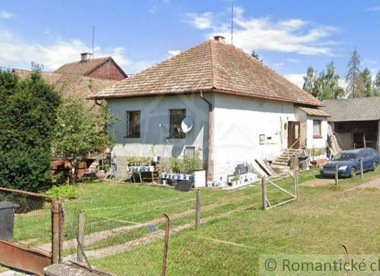 A family house with a traditional roof, a garden with greenery, next to it a farm building, a car.