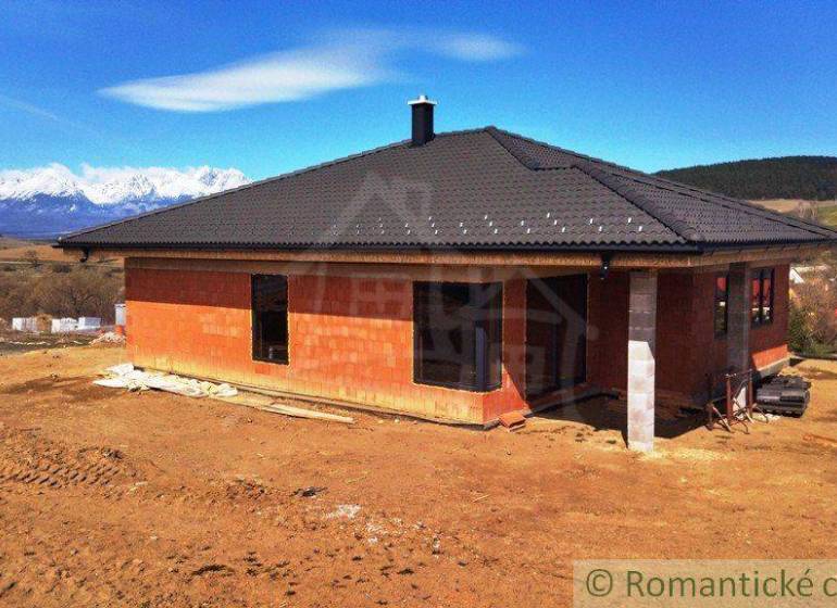 Construction of a family house with a black roof in a picturesque rural setting with mountains.