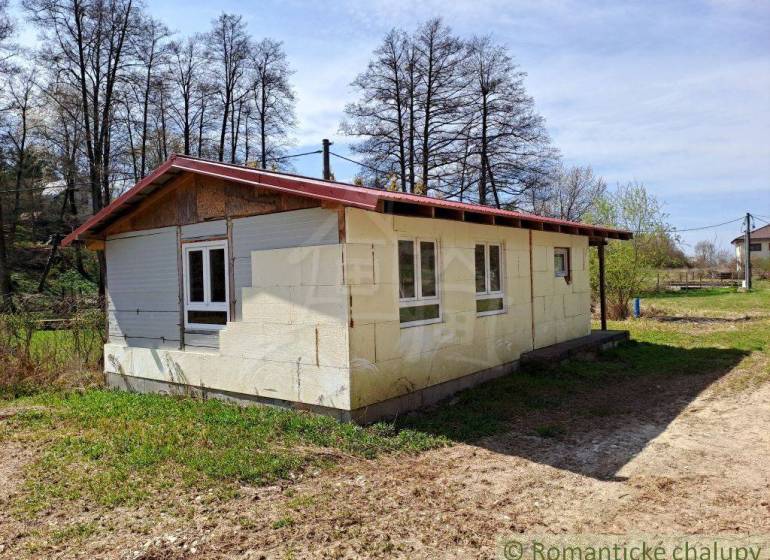 A cottage in nature with a white facade surrounded by grass and trees, an ideal place to relax.