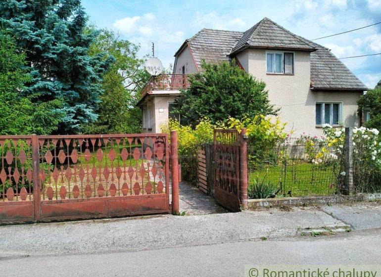 A family house in Košeca with a flower garden and a wooden gate in front of the house.