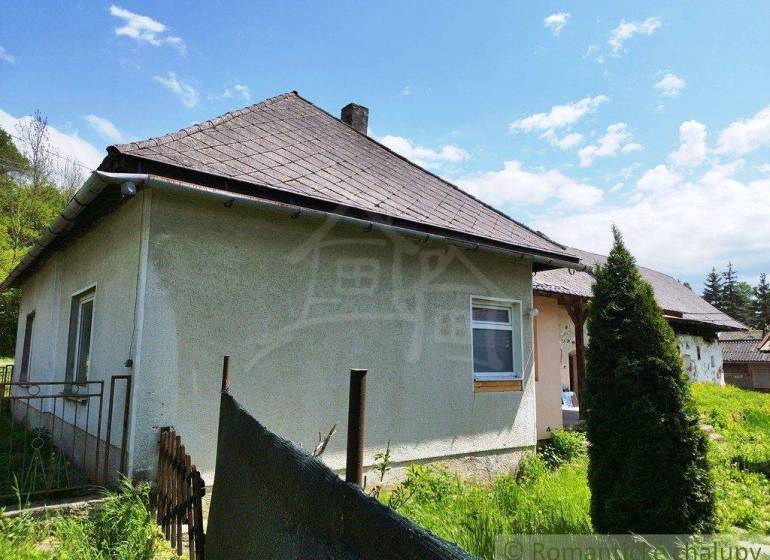 A cottage surrounded by nature with a classic roof and simple fencing.