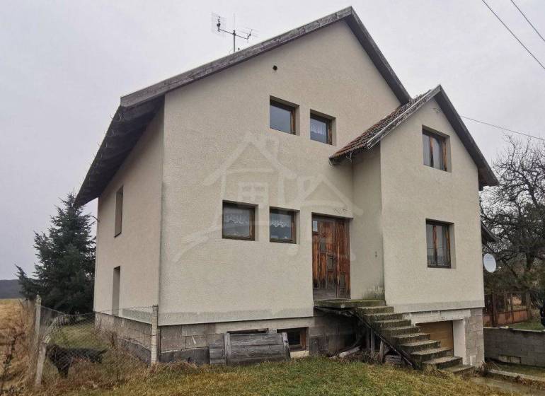 A family house with a concrete foundation, surrounded by a grassy plot, stairs leading to wooden doors.