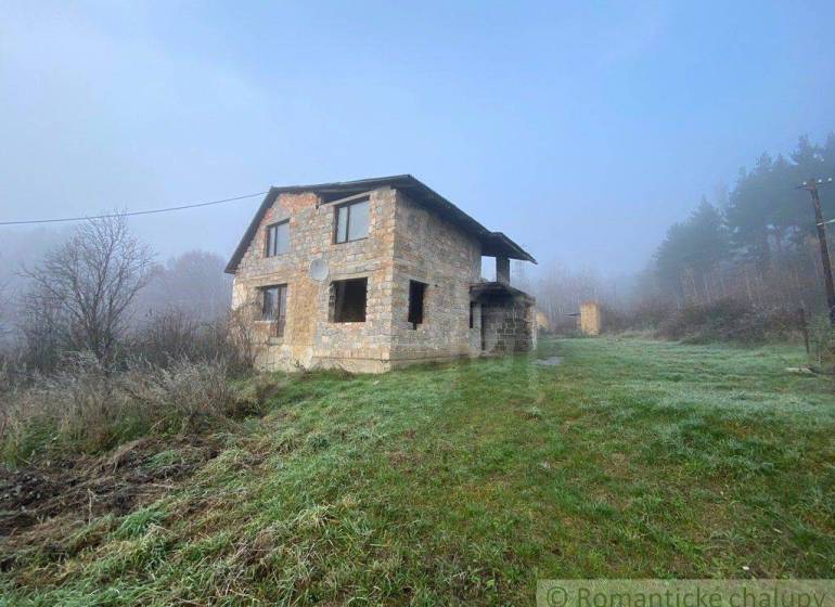 A family house in nature, surrounded by mist and a green meadow near the forest.