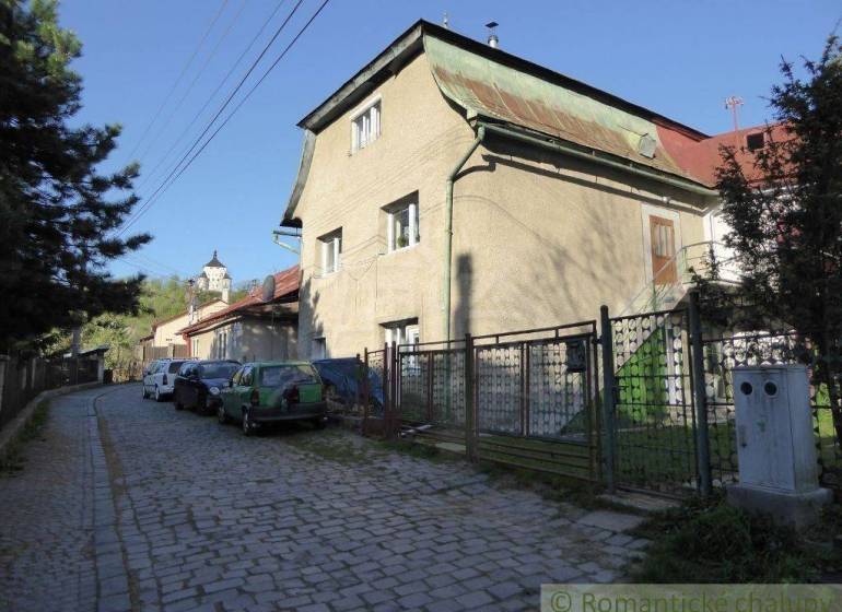 A family house with a metal roof by the road, surrounded by cars and a fence.
