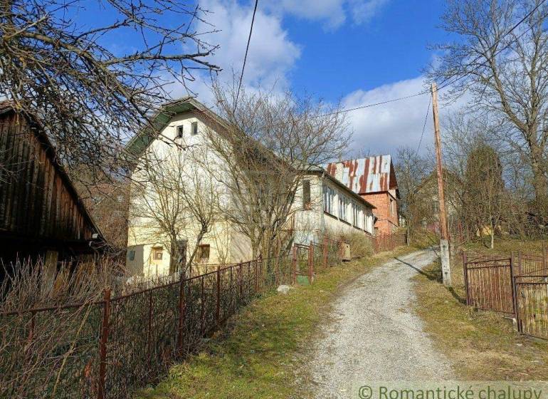 I see an older family house surrounded by nature, a driveway, and a blue sky.