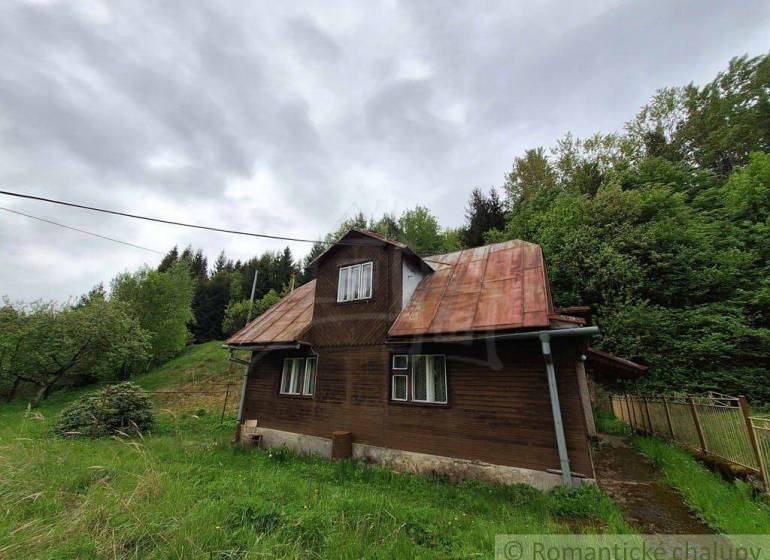 A wooden cottage in Veľké Rovné surrounded by greenery and a slightly cloudy sky.