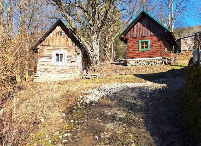 Wooden cottages amidst nature, bordered by trees and a rocky path, in a tranquil area.