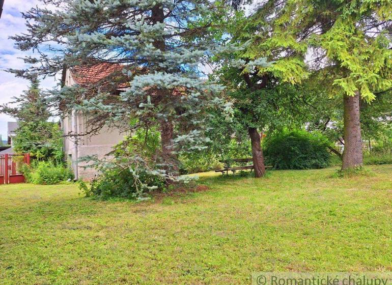 Peaceful residential plots with large trees, a bench, and a house in the background.