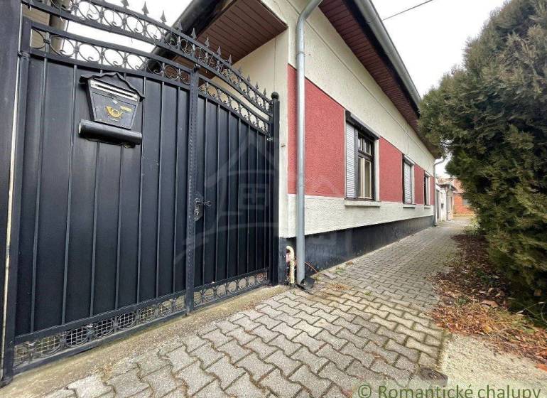 A family house with an iron gate and a small gate stands out with an entrance to a paved walkway.