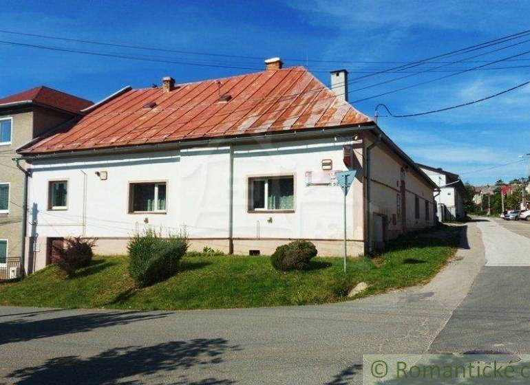 A family house with a red roof, by the road, surrounded by greenery, lies on a slope.