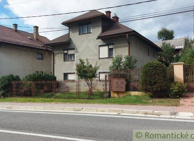 A family house with a garden in a quiet village area, surrounded by a road and a fence.