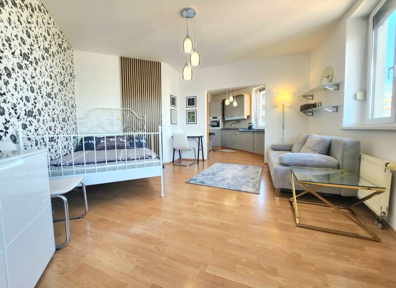 1-bedroom apartment with patterned wallpaper, wooden flooring, kitchen, and seating area.