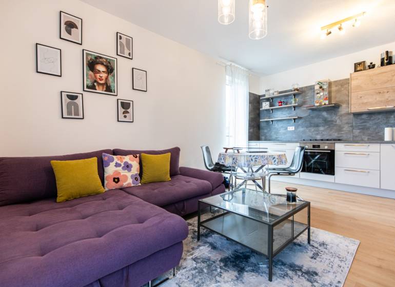 Living room with a purple couch, kitchen, table, and decorations in a 3-room apartment.