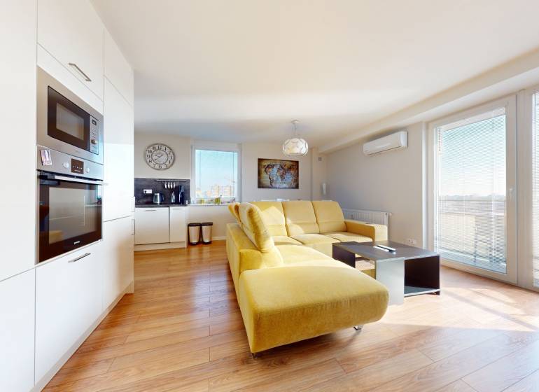Living room with kitchen in a 3-room apartment with a yellow sofa and white furnishings.