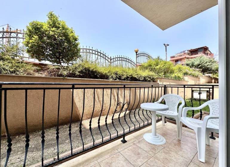 Terrace of a recreational apartment in Nessebar with garden furniture and a view of greenery and a fence.