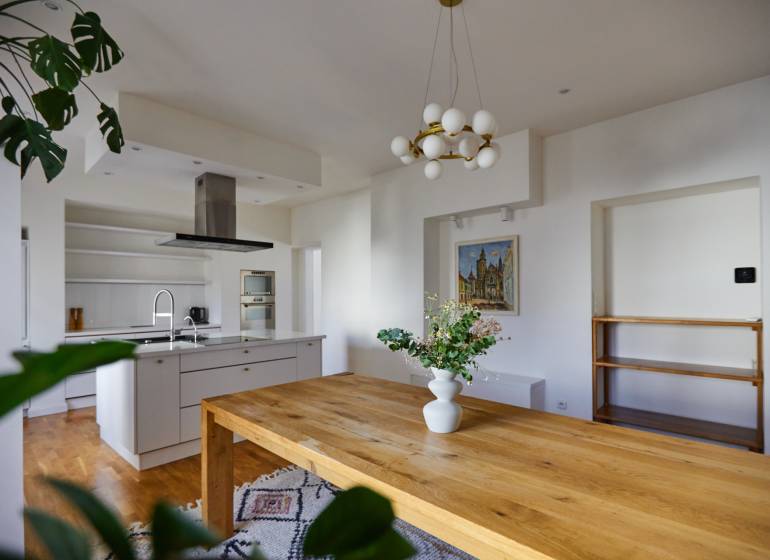 The kitchen of a 4-room apartment with a wooden table, a chandelier, and a decorative vase.