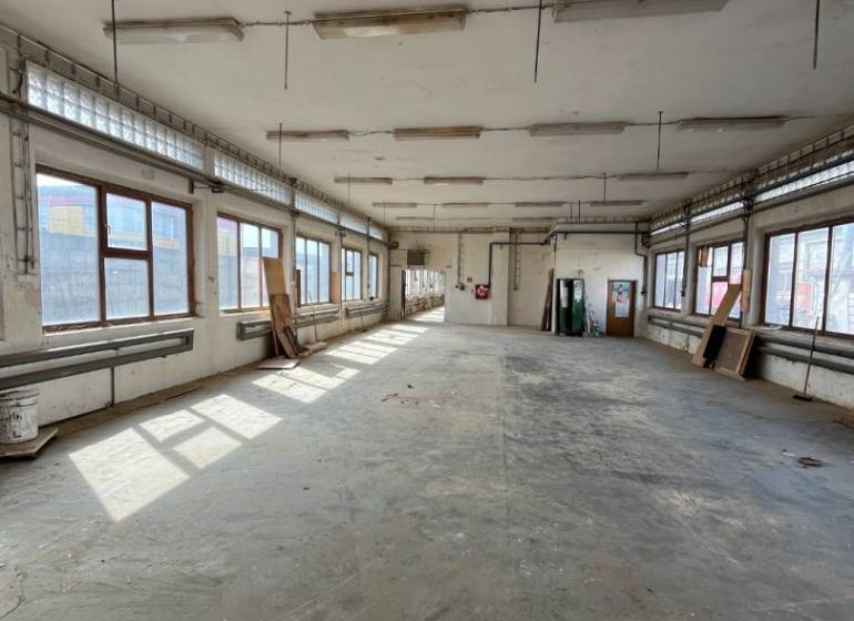 An empty warehouse interior with windows, gray flooring, and hanging lights.