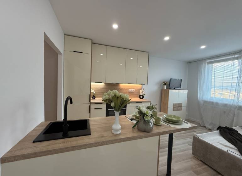 Kitchen of a one-room apartment with a dining counter and a sofa, illuminated by lights.