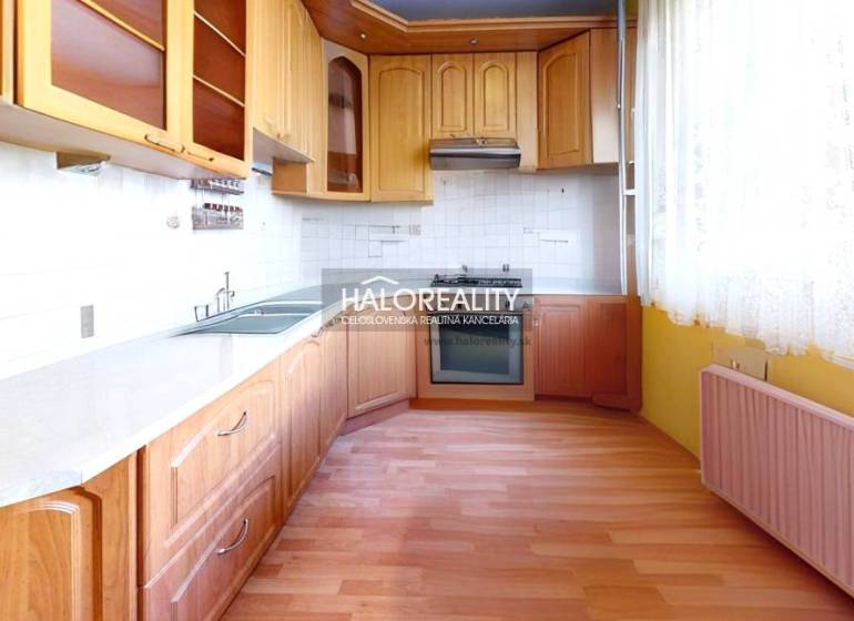 A kitchen with a wooden cabinet and appliances in a 3-room apartment, light tiles, curtains.