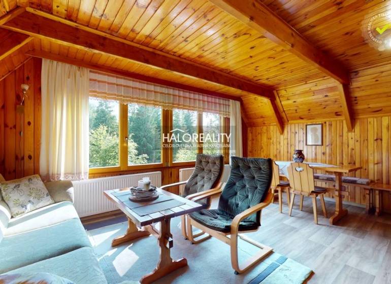 A wooden interior of a cabin with comfortable seating and a view of nature through a large window.