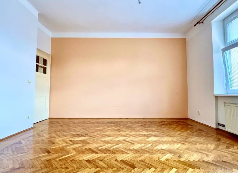 An empty room with a parquet floor and a large window in a two-room apartment.