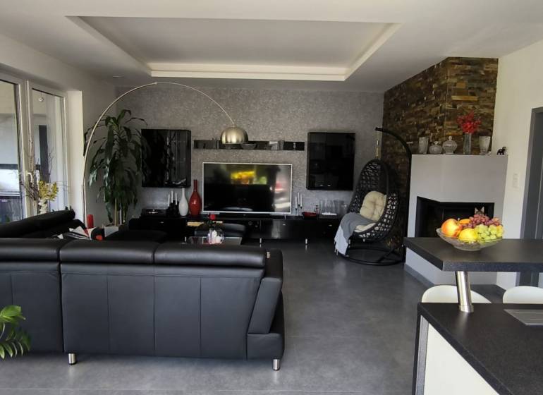 Living room in a family house with black sofa furniture and a TV on the wall.