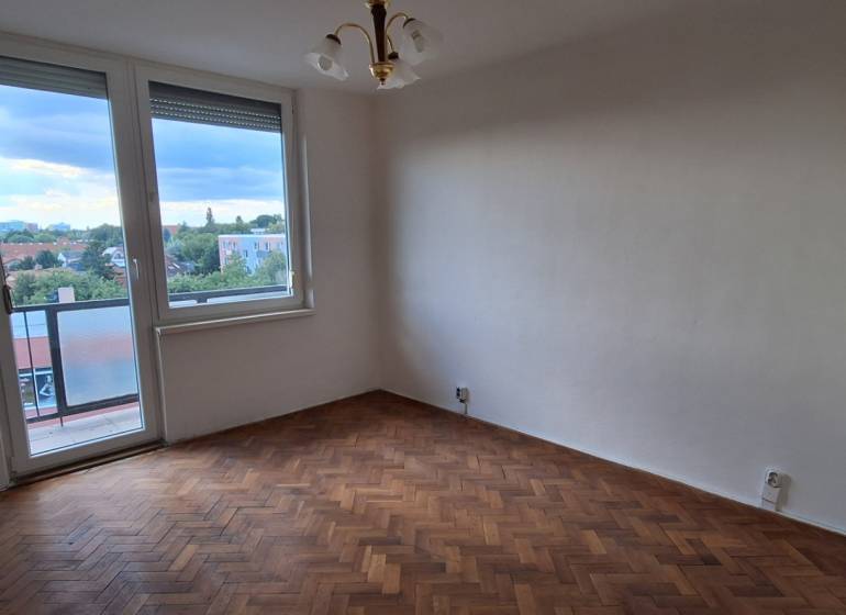 A room in a 3-room apartment with a wooden floor, balcony, city view.