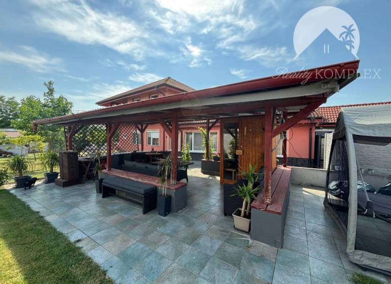 An area with a covered seating by a family house in Trávnik, surrounded by greenery and furniture.