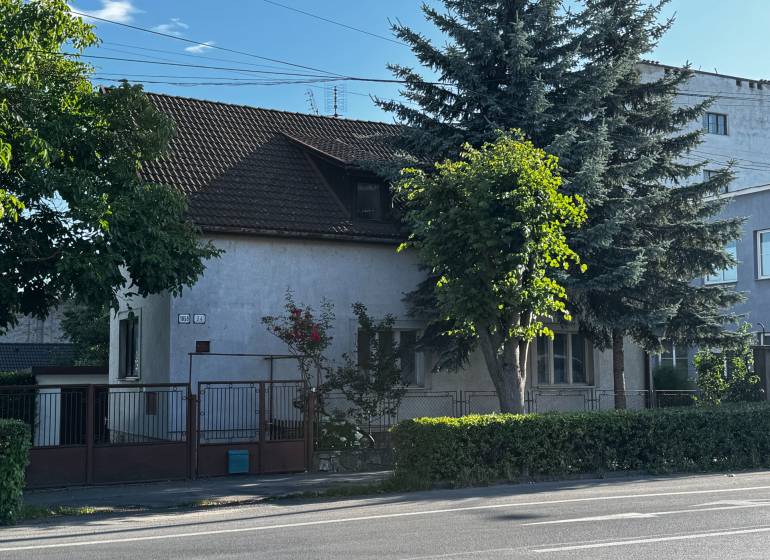 A family house in Lučenec surrounded by trees and a hedge, with access from the main street.