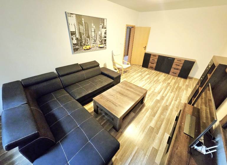 Living room in a three-room apartment with a black sofa and wooden furniture.