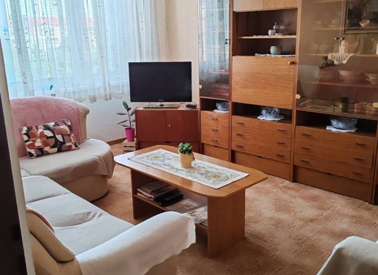 Living room with a sofa, television, and wooden cabinet in a three-room apartment.